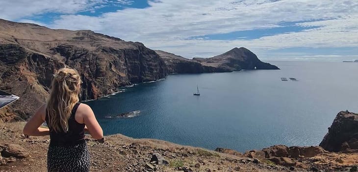 Partner Delivery Consultant Kaitlin Fox with her back to the camera, standing on a cliff overlooking water.