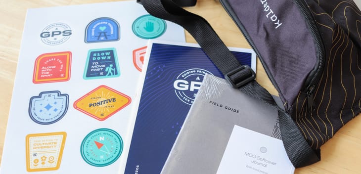 Photo of Kalderos swag featuring a bag, stickers, a GPS document and a “Field Guide” book.