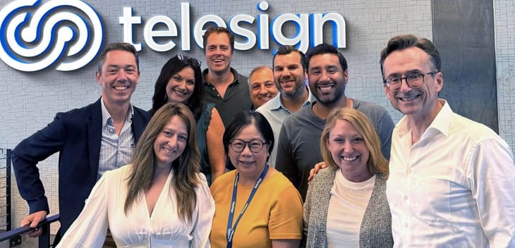 A group of Telesign employees stand together in front of the company sign.