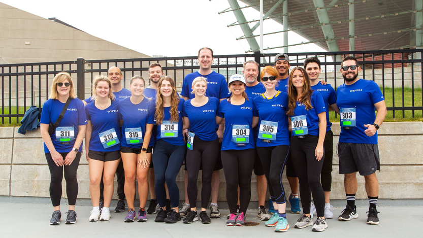 Members of the Wipfli team assemble for an outdoor racing event. They wear matching blue shirts and participation numbers.