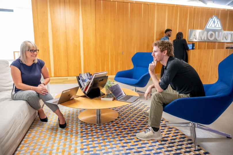 Two Amount team members sit in lobby area, smiling and talking.