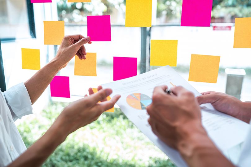 Strategy team using post it notes on glass wall to develop business plan to grow to success