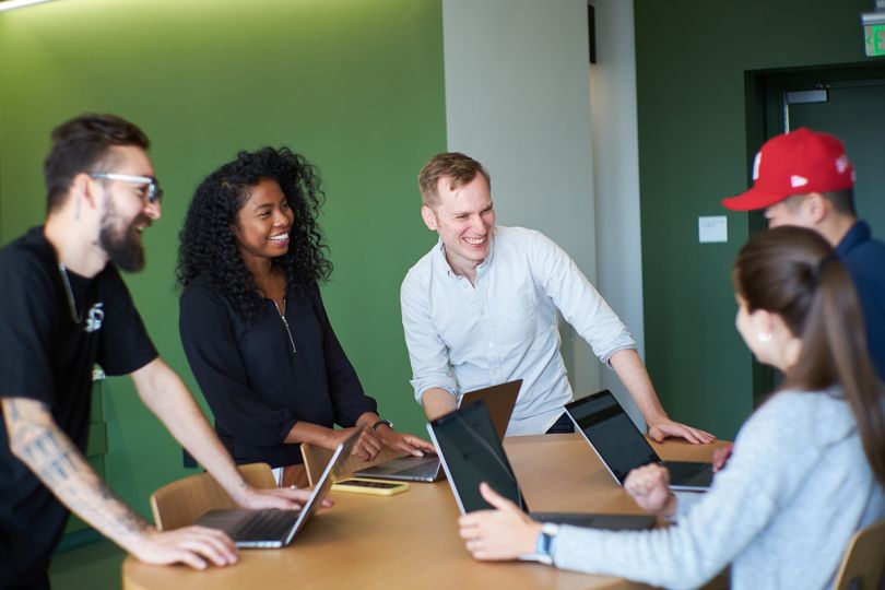 Asana colleagues standing around a table with laptops having a team huddle