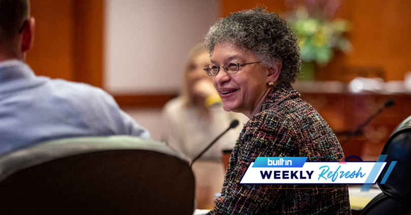 Susan M. Collins, wearing a tweed, multicolored blazer and glasses. She has short curly hair and round glasses.