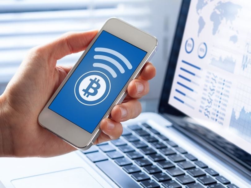 A person conducting a cryptocurrency transaction on their phone and computer