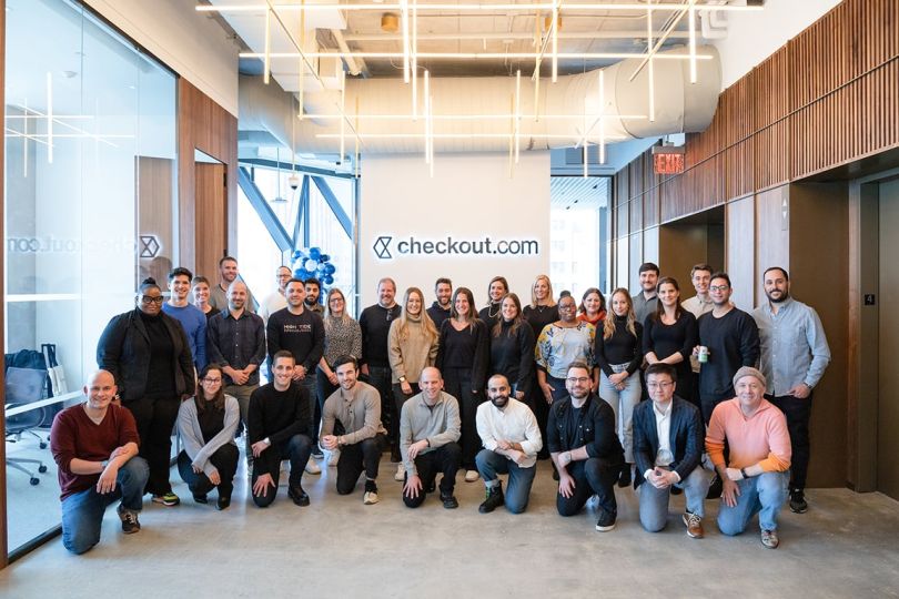 Checkout.com team photo in the office with the company logo on the wall behind them
