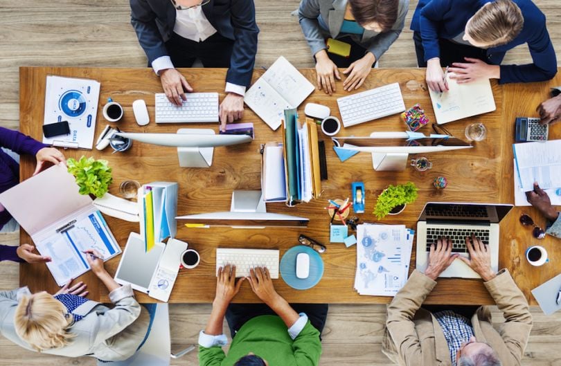 Numerous employees around a table working 
