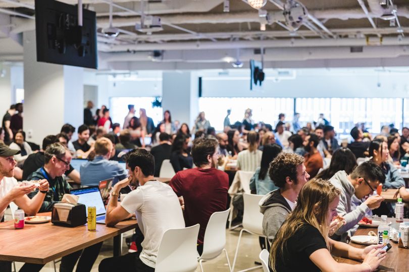 A room packed with employees, sitting at tables and having lunch.