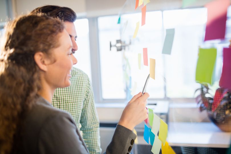 Coworkers in office sharing ideas with post it notes on the wall