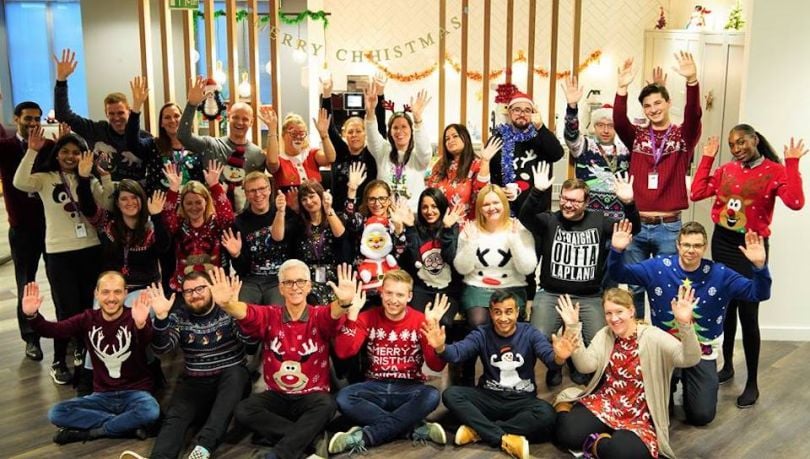 Ensono staff at in holiday seaters raising their hands