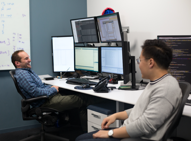 Two Geneva Trading staff chatting at their desks
