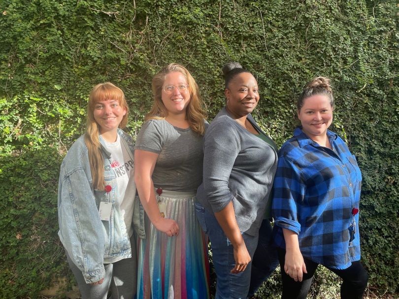 AWL group photo of four employees in front of a hedge wall