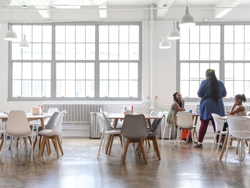 Three people gather around a table in the corner of a large, brightly lit dining room.