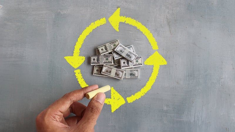 A circle of arrows drawn around a pile of money.