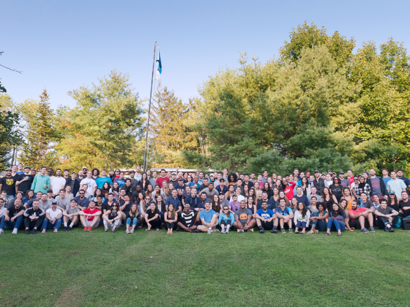 A large group of people sits outside in the grass