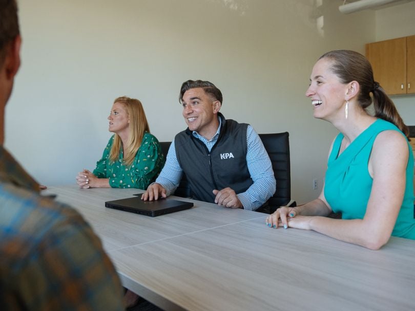 Trevor Stage sits in front of a closed laptop as he talks with coworkers