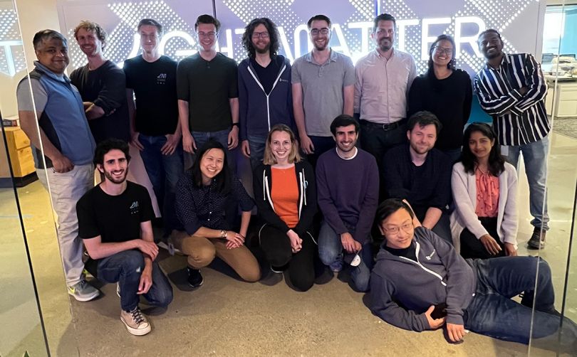 Lightmatter team photo in the office with a company logo neon sign behind them