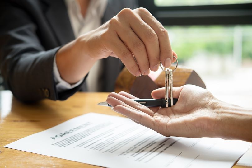 Real estate agent holding house key to his client after signing contract agreement in office
