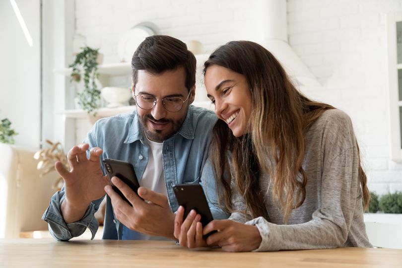 Two people sitting at a table at home looking at their mobile phones