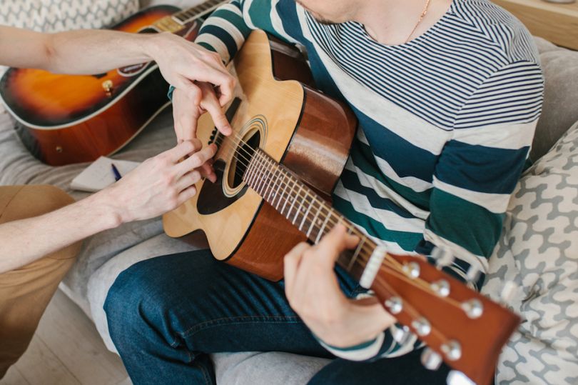 Person guiding another persons hands playing guitar