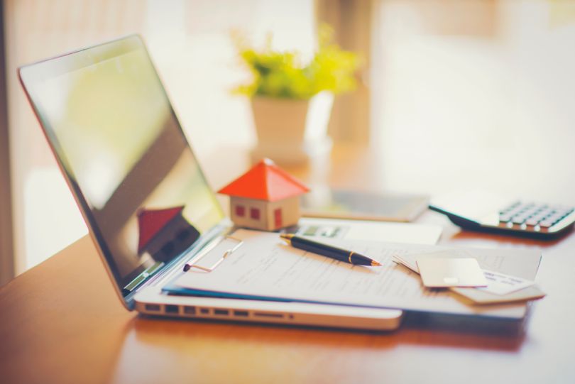 A laptop on a desk with paperwork, credit cards and a house made from paper