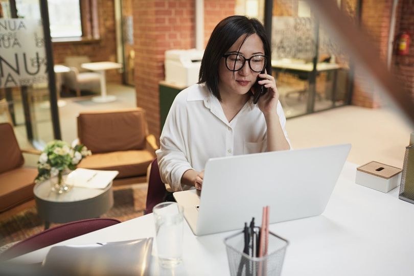 businesswoman sitting at workplace in modern office and speaking by phon