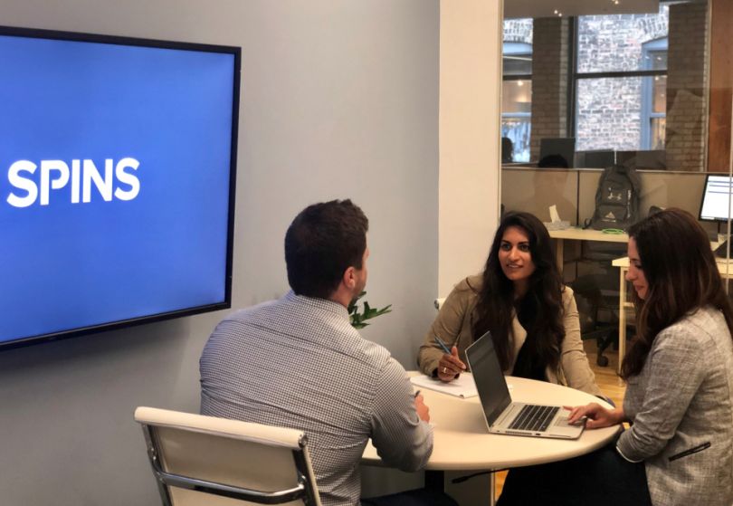 SPINS team member chatting next to a TV screen