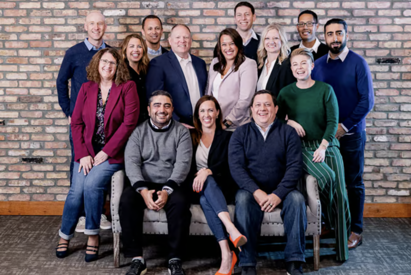 14 people seated and standing in front of a brick wall