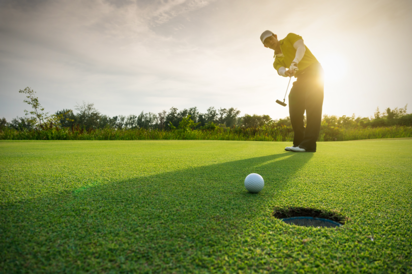 A golfer wearing a visor puts on a green.