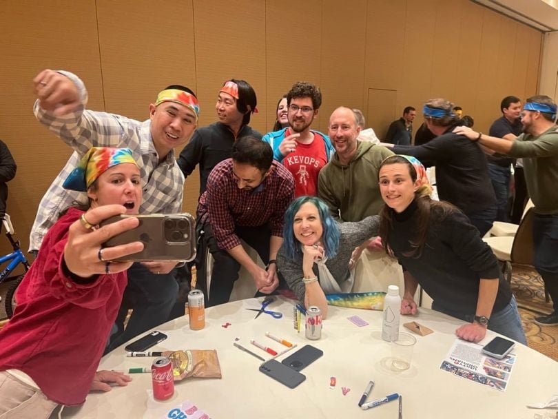 Candid photo of eight team members posing for a selfie around a table with markers wearing colorful items