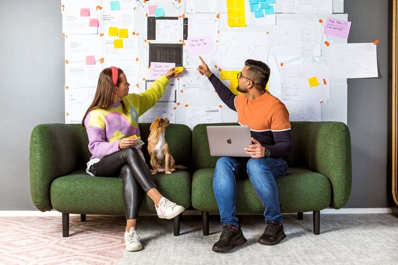 Two Smartly team members sitting on a couch sharing ideas pointing to post it notes on the wall behind them