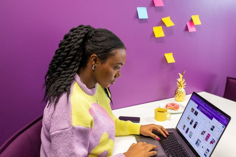 Smartly.io team member sitting at a desk working on a laptop with post it notes on the wall