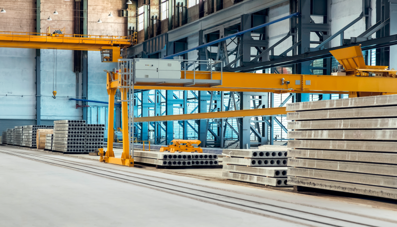 Cement manufacturing floor with pallets of cement bricks piled up and yellow cross-beams going across the space.