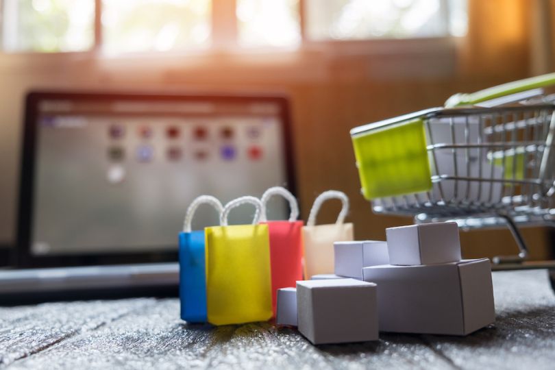 Miniature shopping cart and shopping baskets in front of laptop