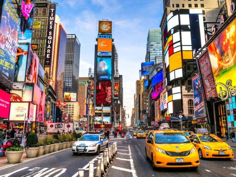 Cars rush past in bustling, colorful Times Square