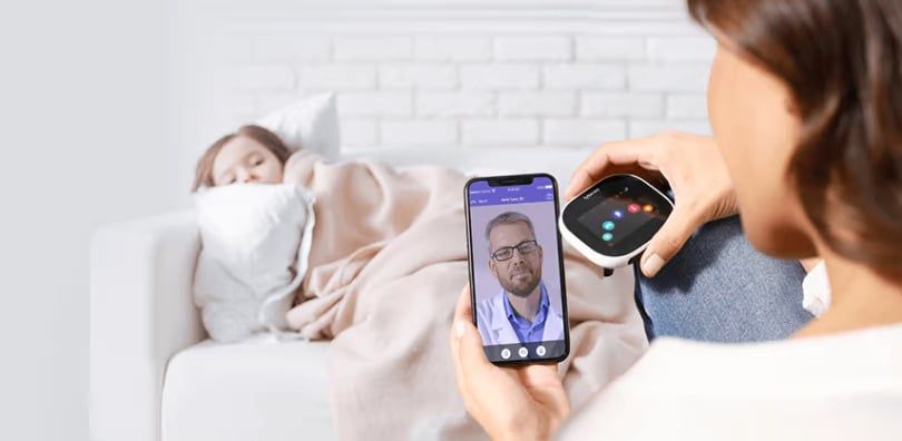 Mother with a sick child taking to a doctor via a video chat on a mobile phone
