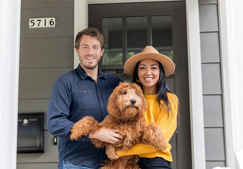 A couple holding a puppy in front of their home. 