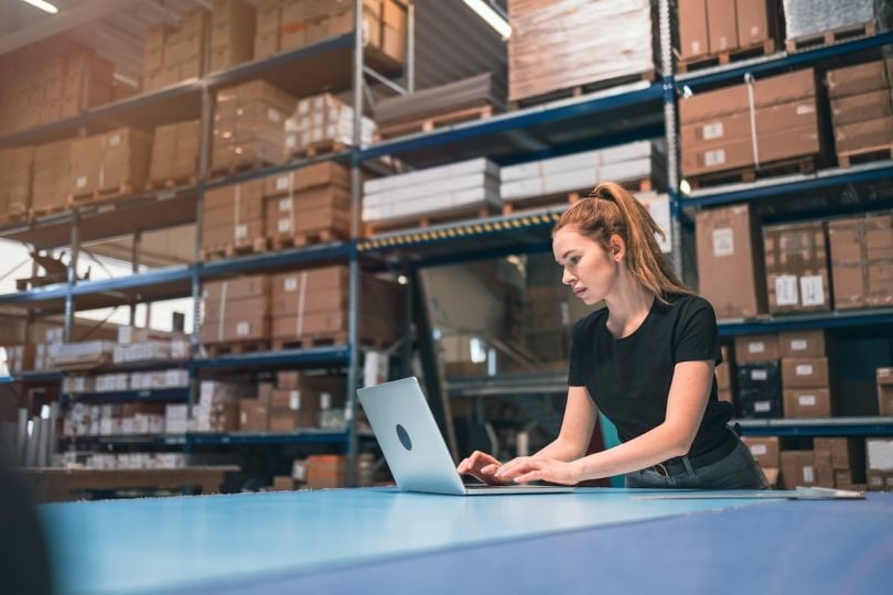 A woman in a retail stock facility uses a laptop