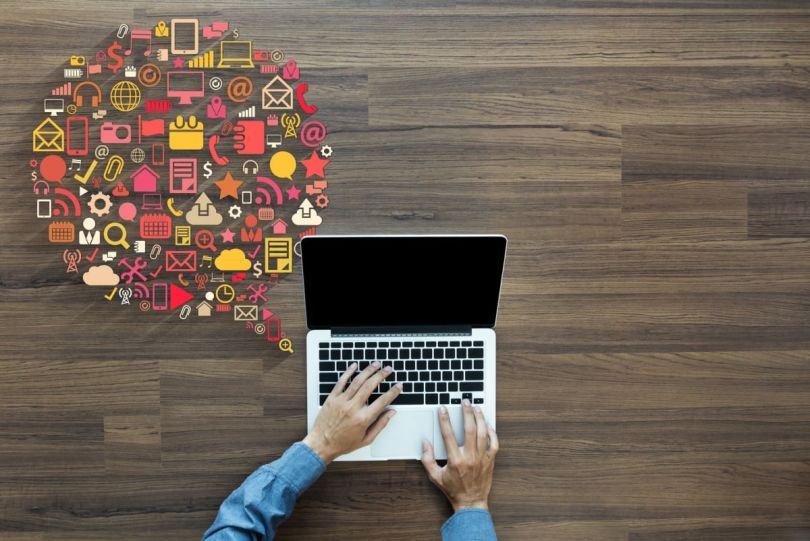 A person’s hands on a laptop keyboard with an array of colorful digital media and communication icons bursting from the screen.