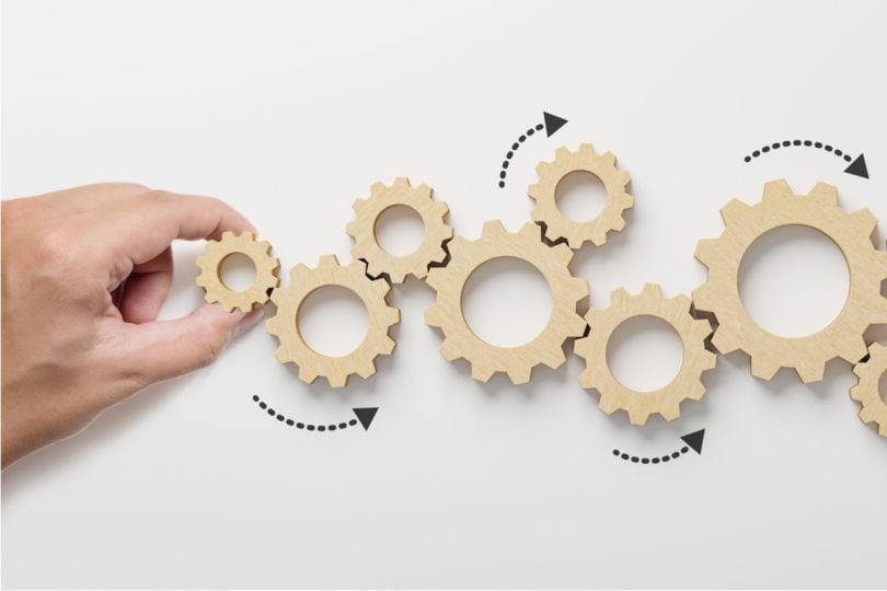 A hand placing a wooden gear into a sequence with other gears.