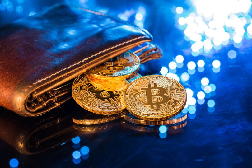 Gold coins bearing the Bitcoin symbol are pictured falling out of a wallet.