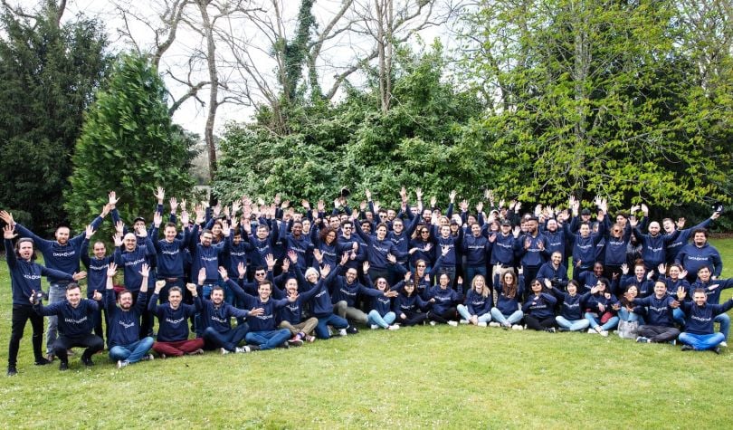 DataDome employees wearing blue DataDome sweatshirts stand in the grass surrounded by trees.