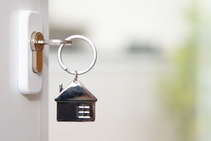 A key in a door lock with a keychain shaped like a house.