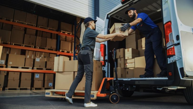 A delivery person hands boxes to someone, reflecting delivery logistics.&nbsp;