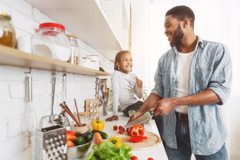 A father and daughter cheerfully prepare a meal together in a brightly lit kitchen.&nbsp;
