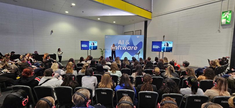 Event photo of GitLab leader standing on a stage in front of a seated audience, with a backdrop that reads “AI & Software.”&nbsp;