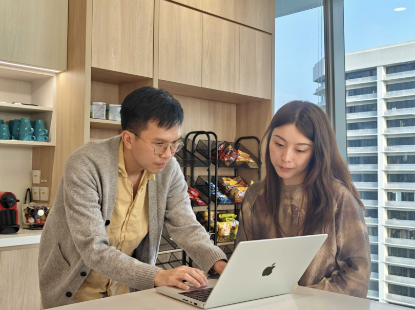 Two Airwallex employees view information on a computer laptop screen while working together in a kitchen area in one of Airwallex's offices.