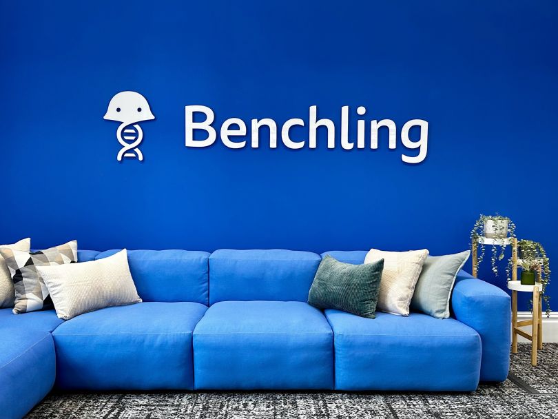 Image of a blue couch situated against a blue wall with the Benchling logo on it in the company’s Belfast office