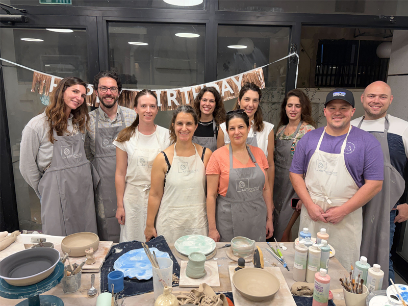 Several Bring team members pose for a group photo while wearing aprons during a pottery-making class