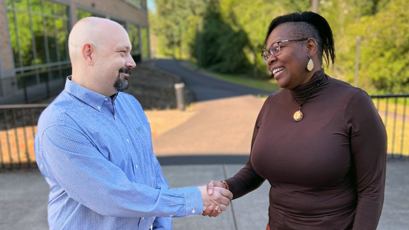 Brian and Rakiah shake hands, smiling, outside Fisher Investments’ office.&nbsp;
